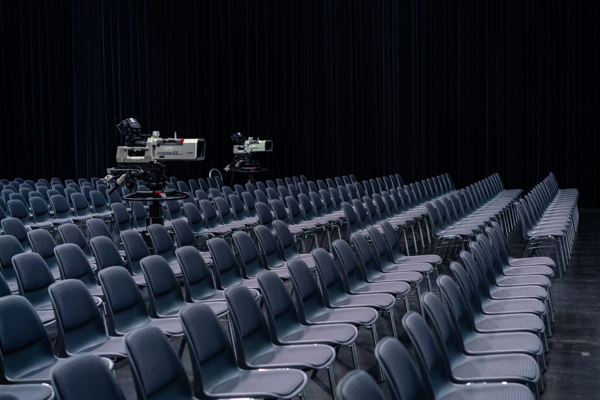 Empty rows of seats in a darkened auditorium, two broadcast cameras set up mid-floor